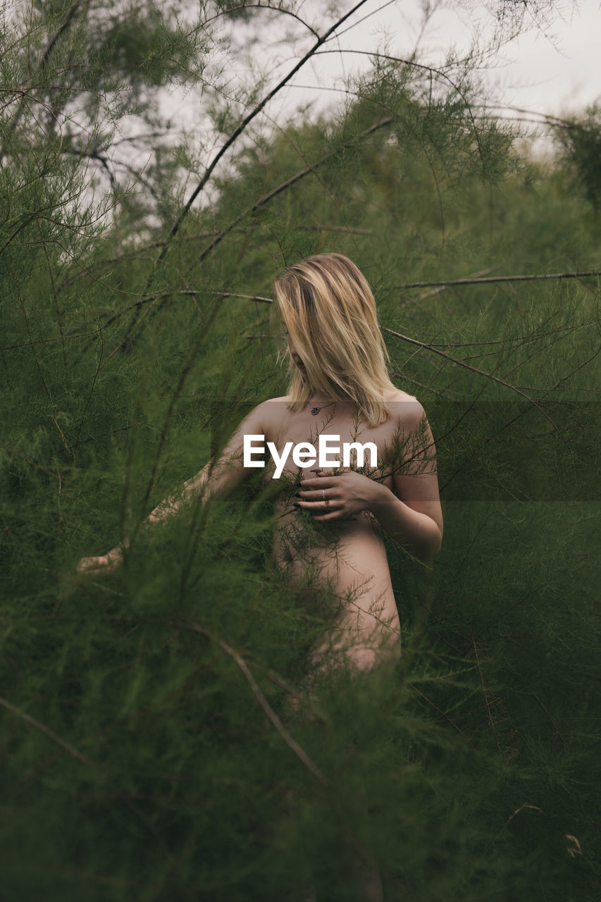 Naked woman standing amidst plants