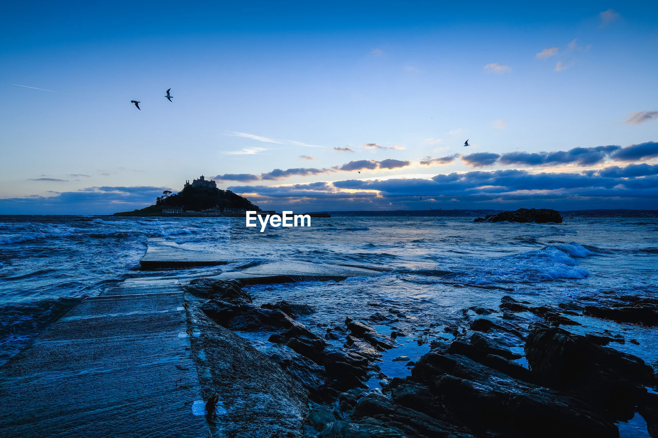 BIRDS FLYING OVER SEA AGAINST SKY