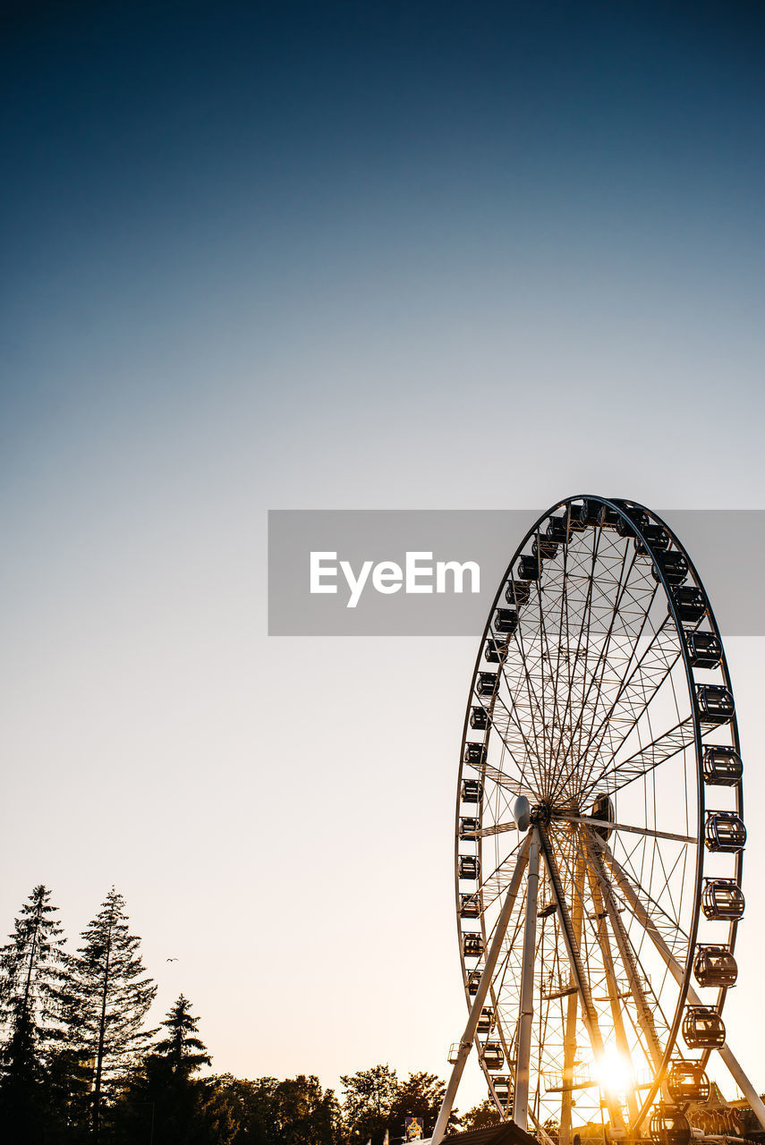 LOW ANGLE VIEW OF FERRIS WHEEL AGAINST CLEAR SKY AT DUSK