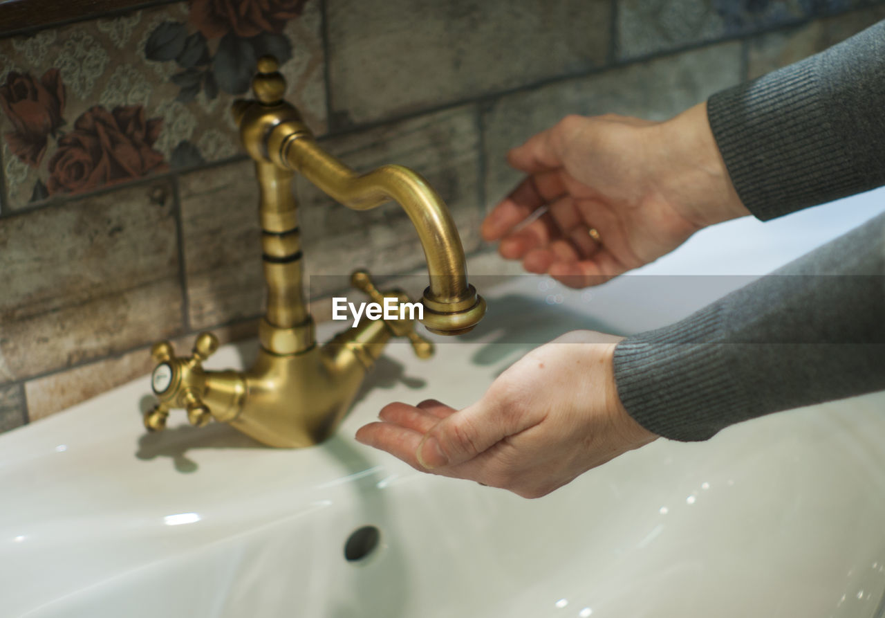 Cropped hands of woman washing hands in sink