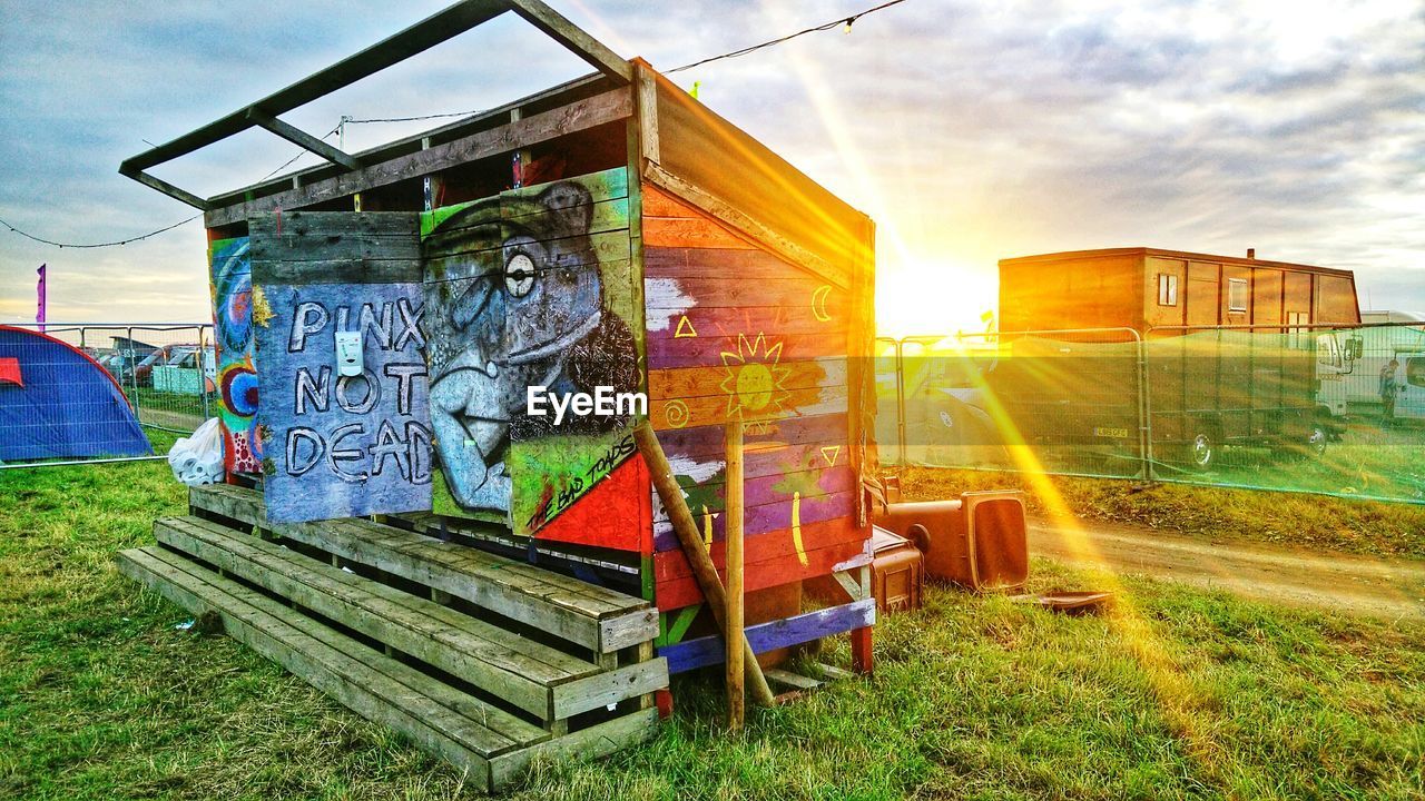 Graffiti on public restroom grassy field against cloudy sky during sunset