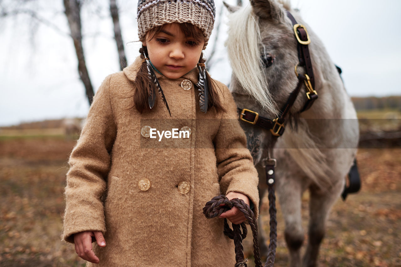 Beautiful girl leading her pony by bridle