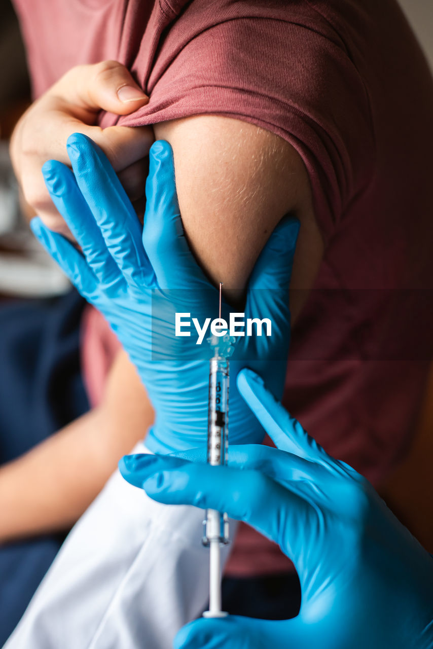 Close up of teenager getting vaccinated by doctor holding a needle.