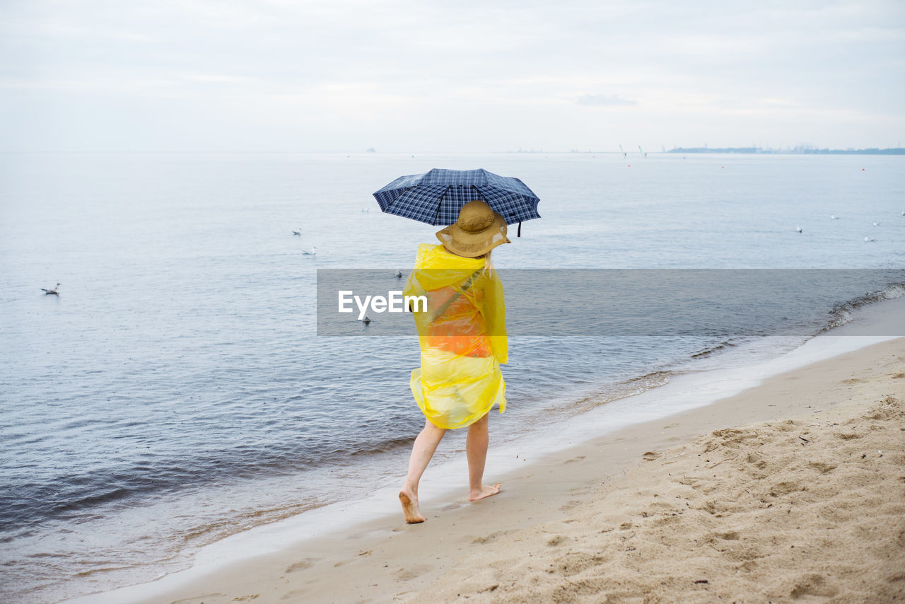 Woman with umbrella walking at sea shore