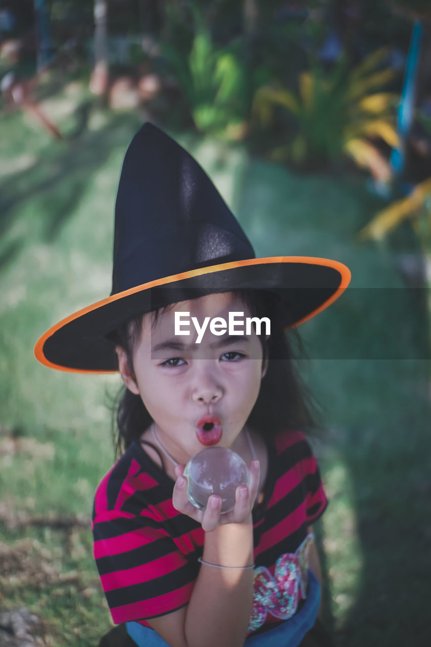 Portrait of girl wearing witch hat holding crystal ball