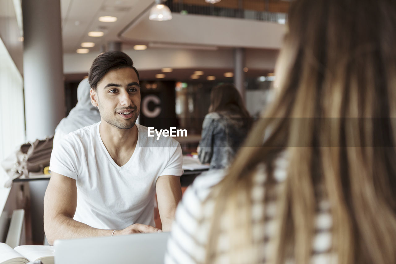 Smiling man discussing with female friend while studying in high school