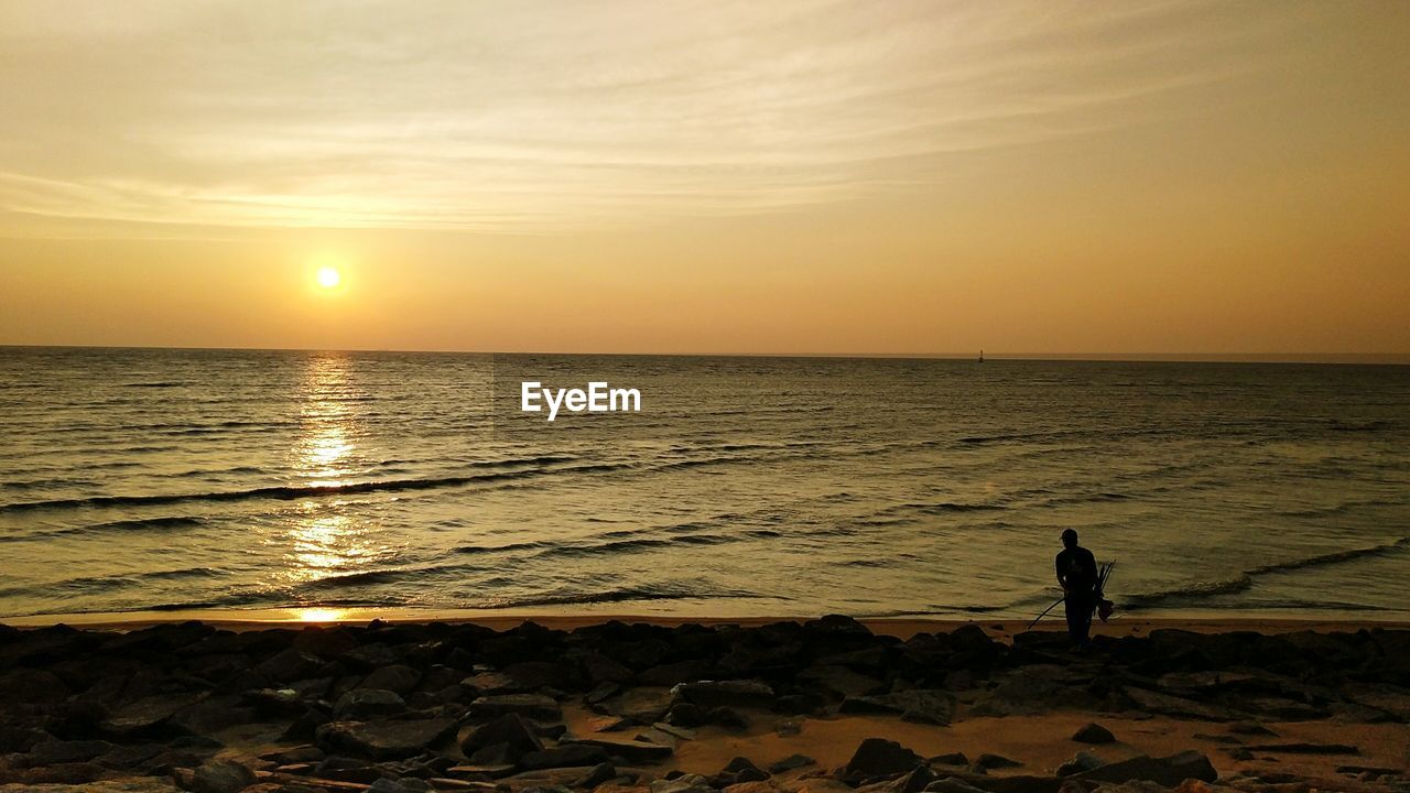 Silhouette man at beach against sky during sunset