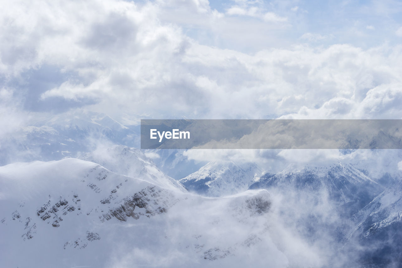 Aerial view of snow covered mountains against cloudy sky