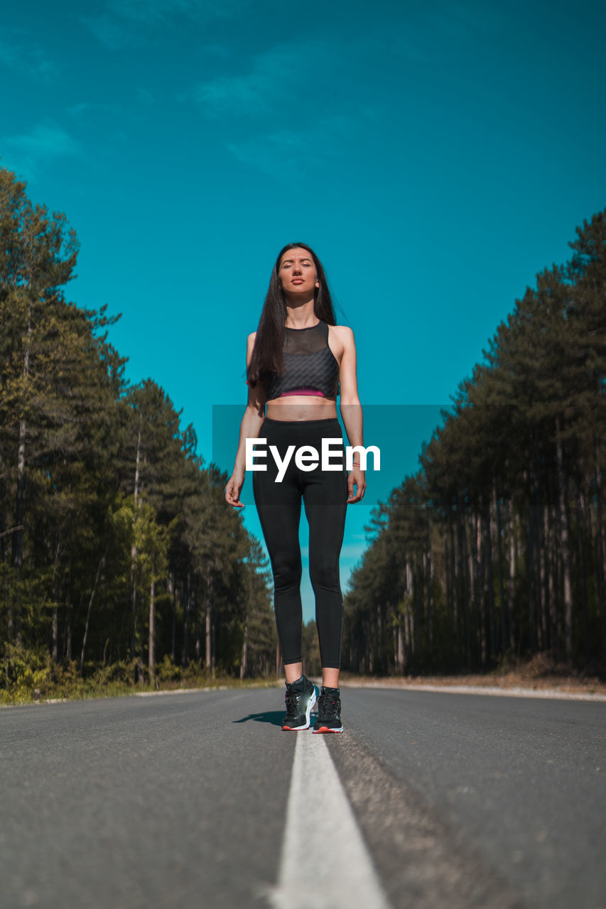 Full length portrait of woman on road against trees