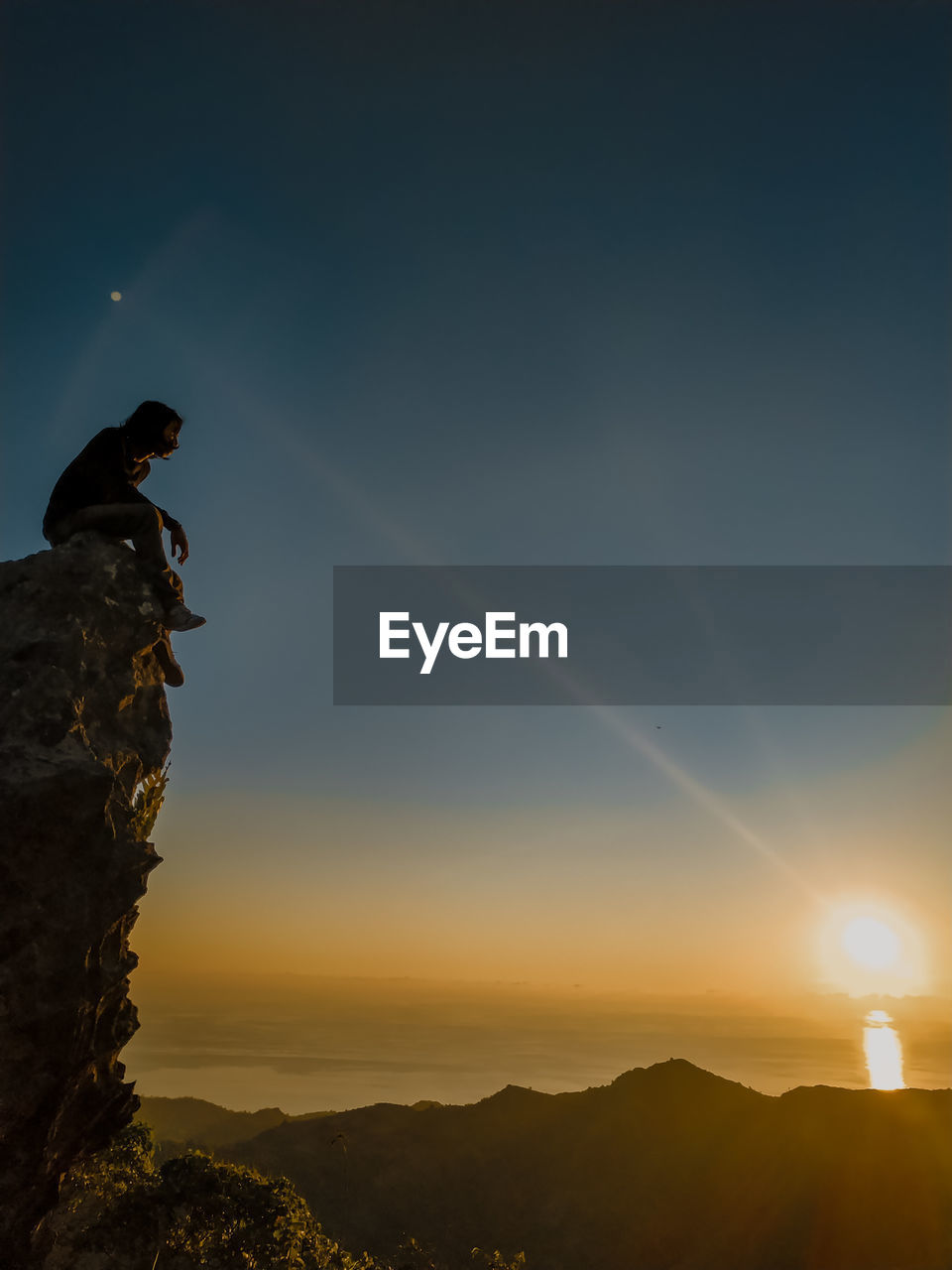 SILHOUETTE MAN ON ROCK AT SUNSET