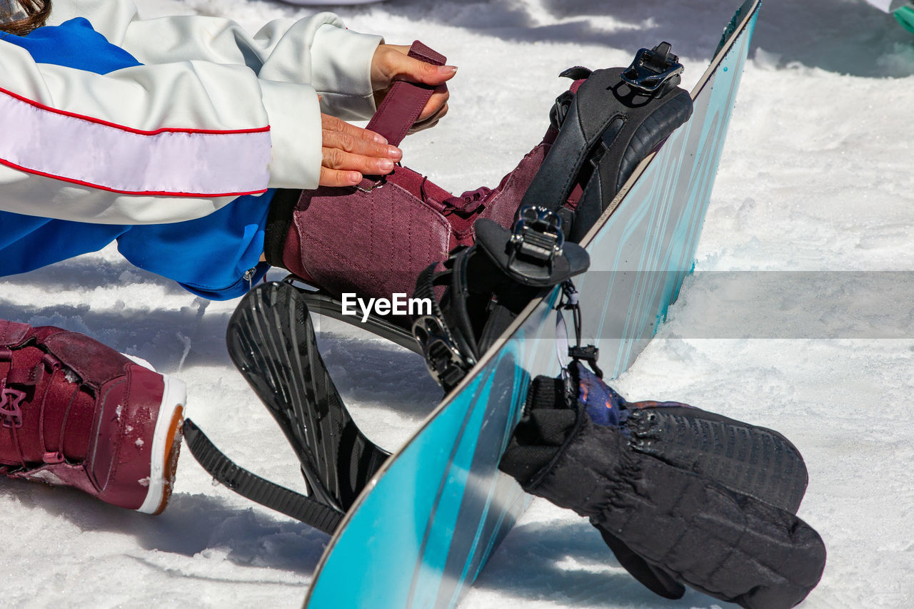 Low section of man wearing snowboard sitting on snow