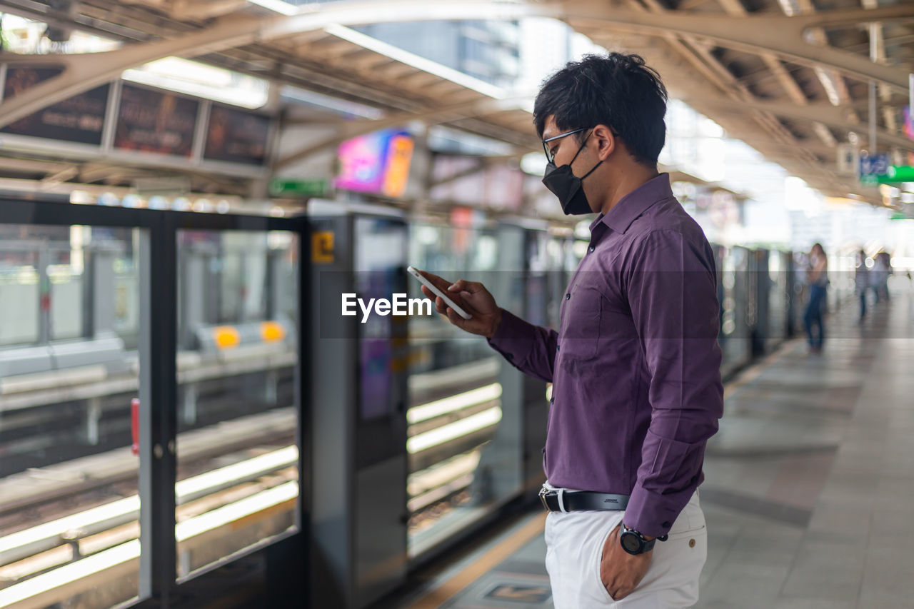 Young asian man using smartphone while waiting for subway or sky train.