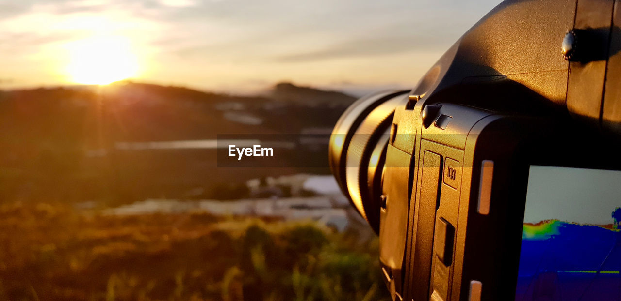 Close-up of camera against sky during sunset