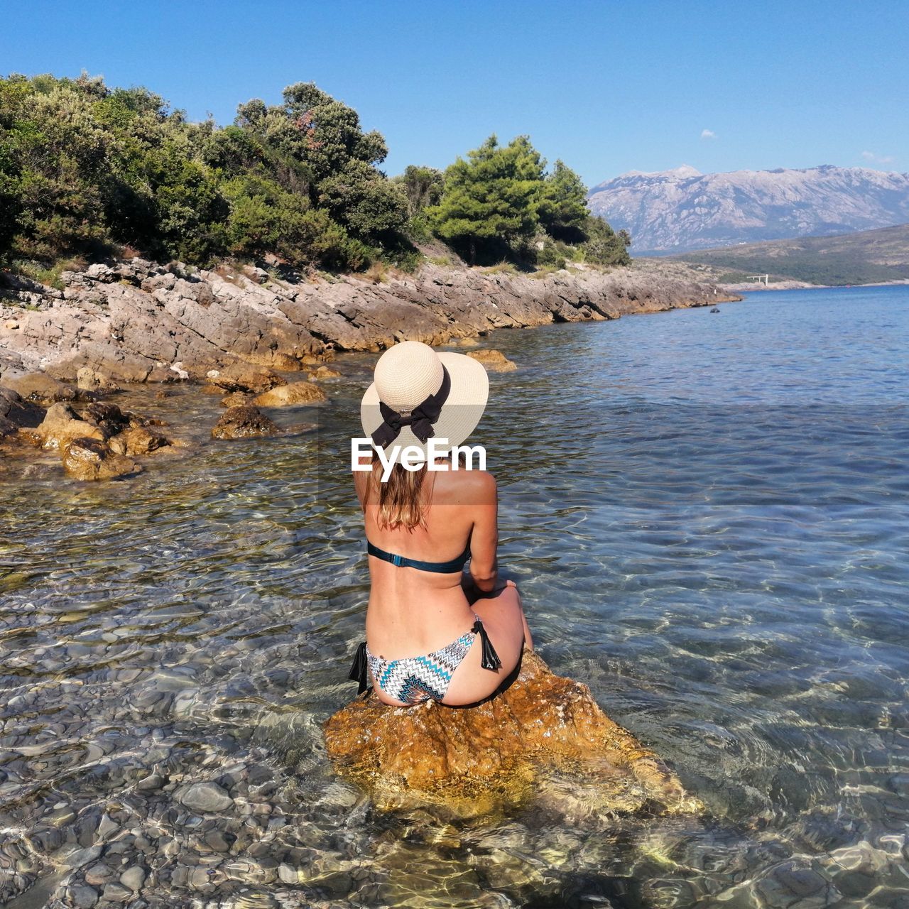 Rear view of woman sitting on rock in lake