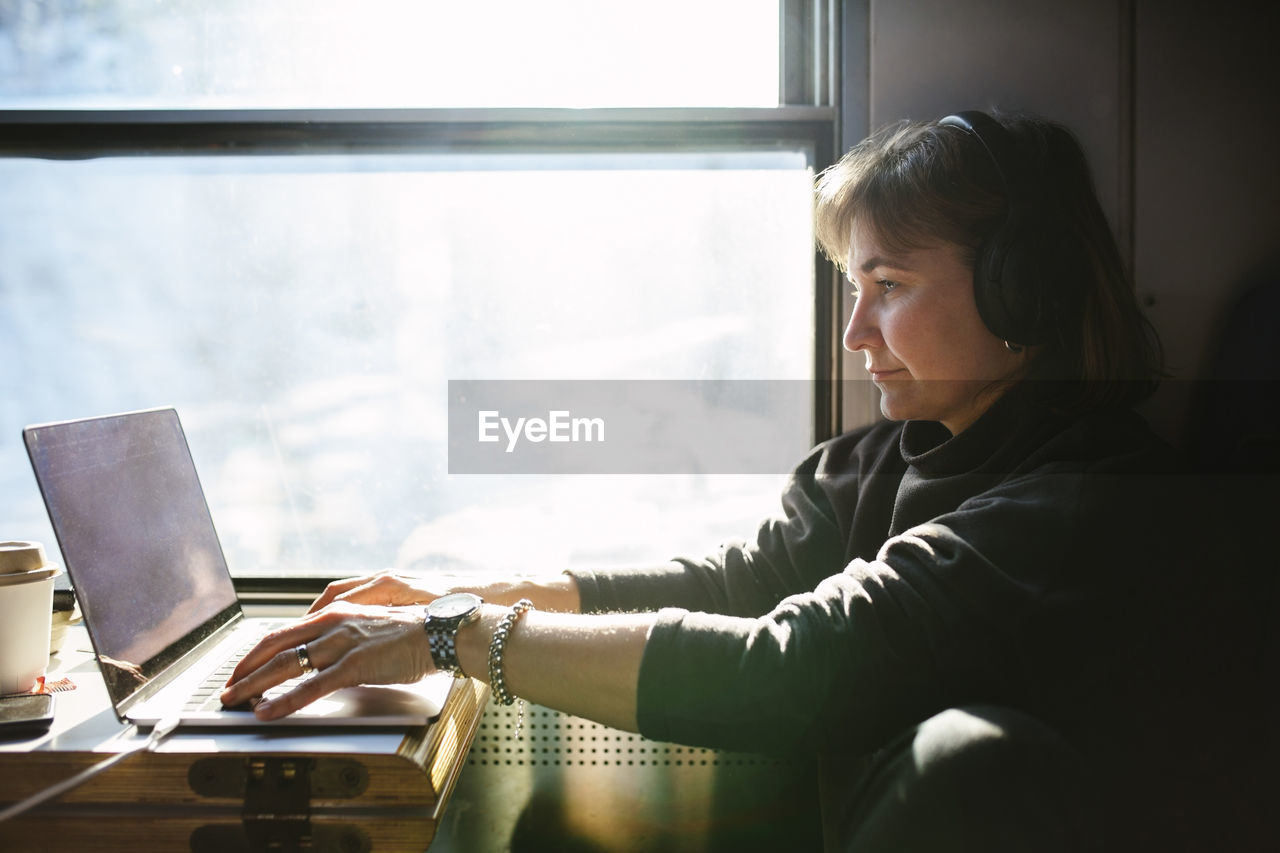 Businesswoman using laptop while sitting by window in train