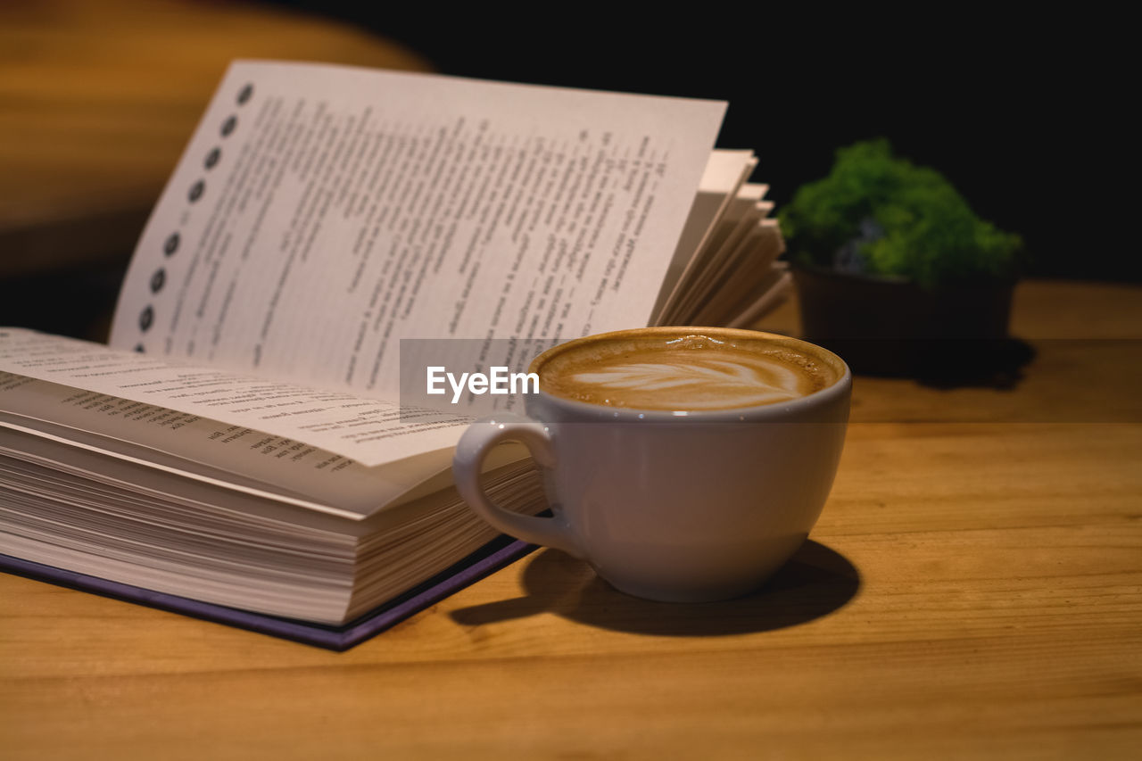 CLOSE-UP OF COFFEE CUP ON TABLE AGAINST BOOK