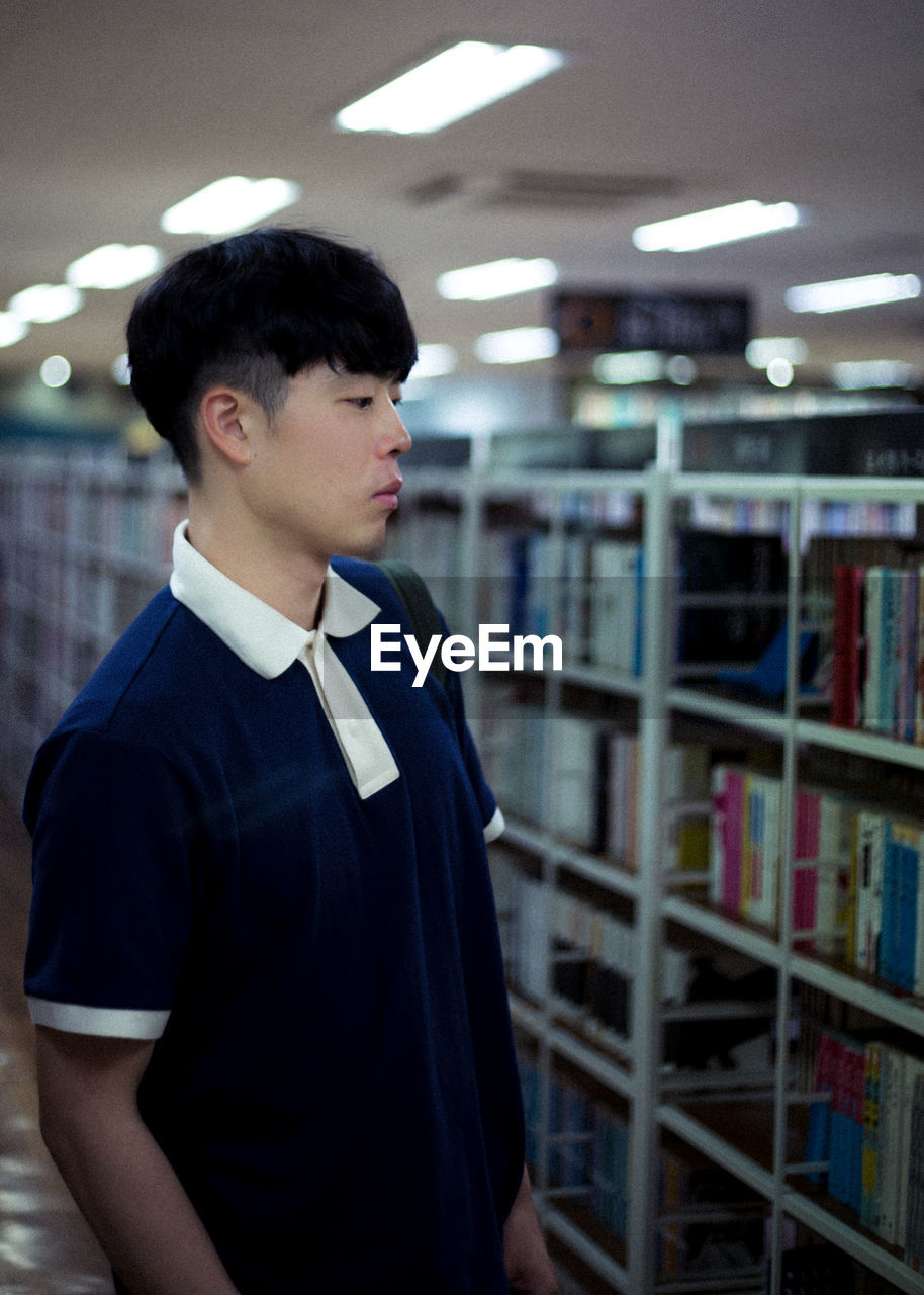 Side view of young man standing in library