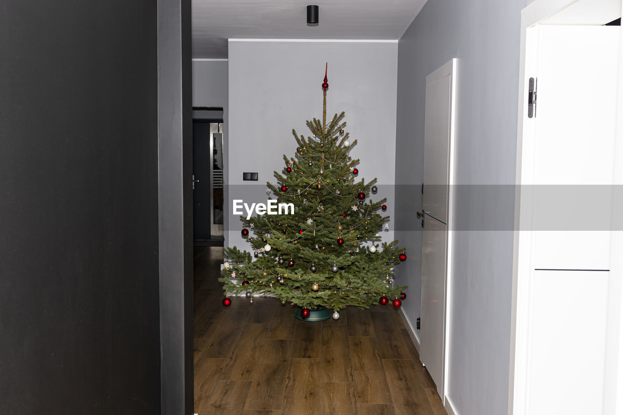 A spruce christmas tree decorated with baubles standing in the hall of a modern house.christmas tree