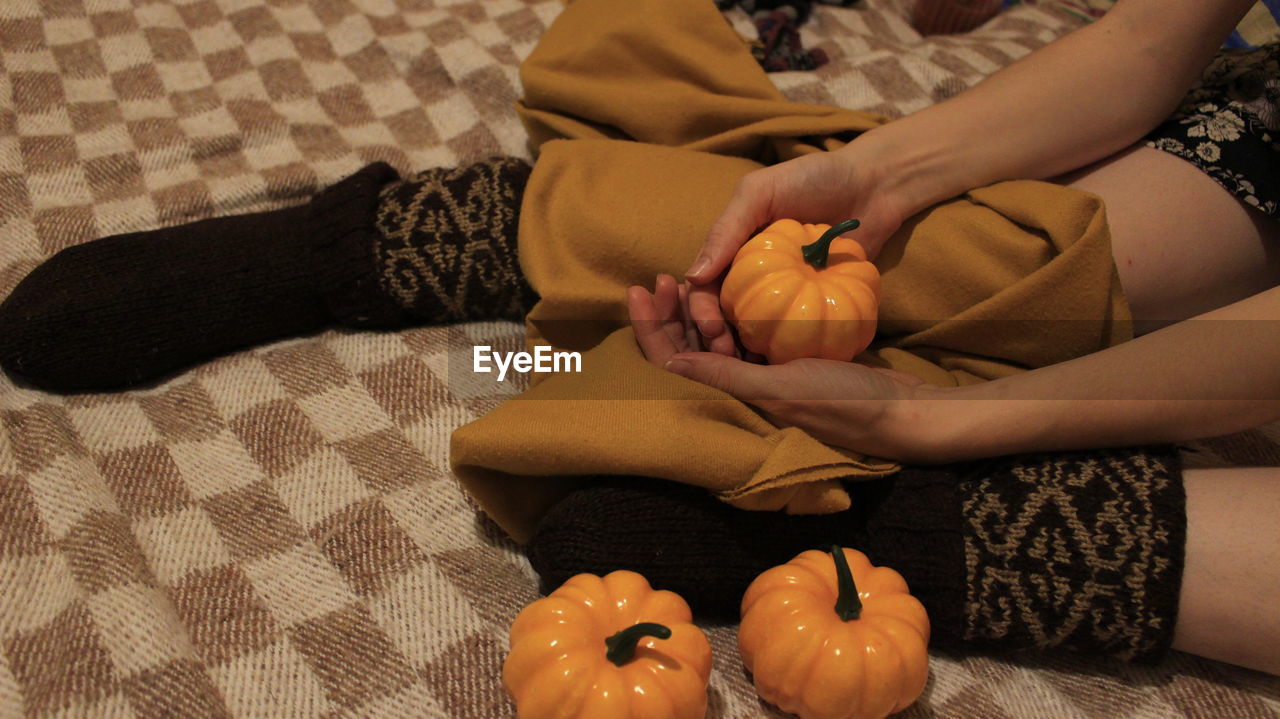 Low section of woman holding toy pumpkins while sitting on bed at home