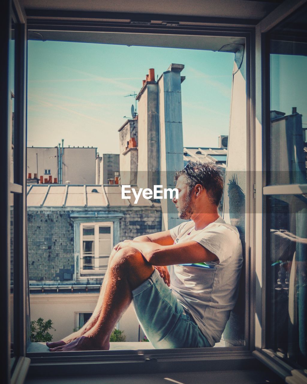 Man sitting on window sill in city