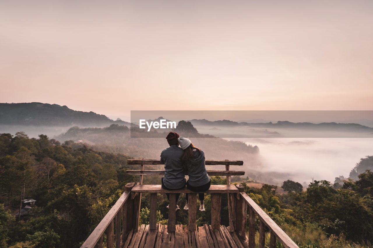 PEOPLE LOOKING AT MOUNTAIN AGAINST SKY AT SUNSET