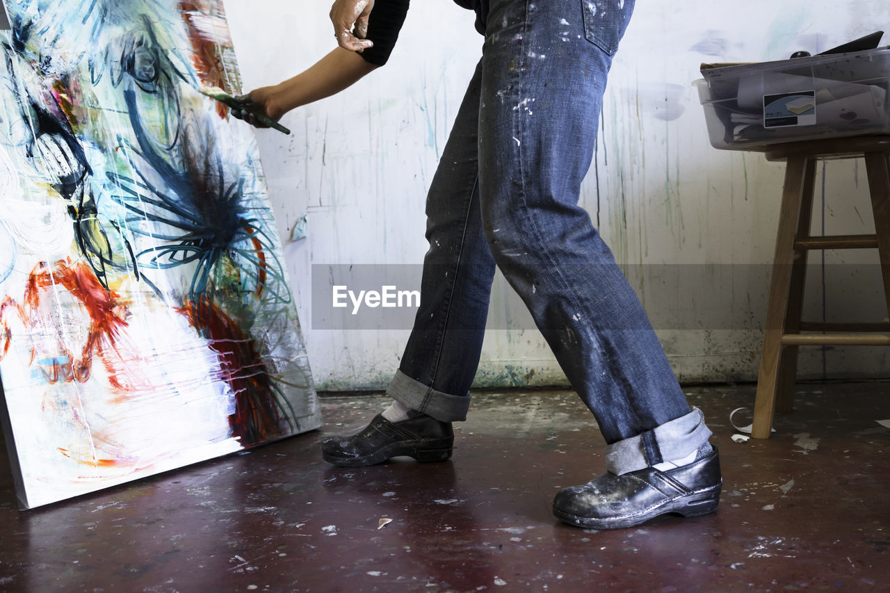 Low section of woman painting on canvas in art studio