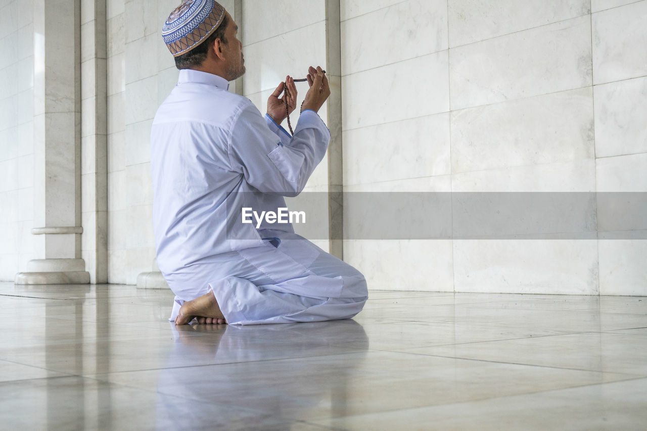 Man holding prayer beads while praying at mosque