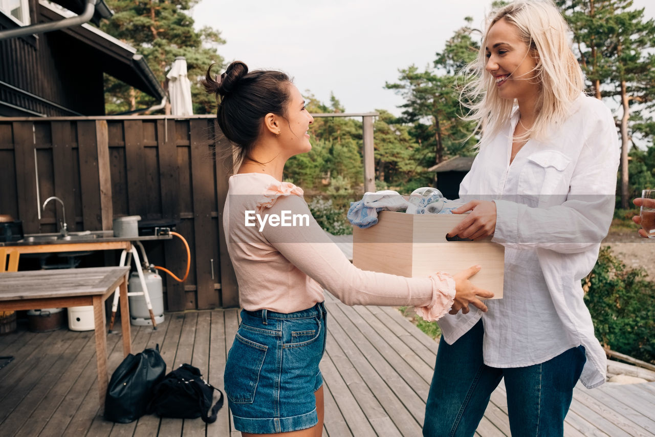 Smiling young woman giving wooden container to friend