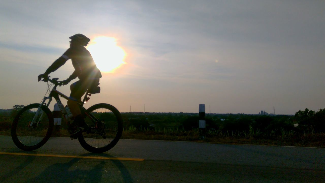 MAN RIDING BICYCLE ON ROAD AGAINST SKY