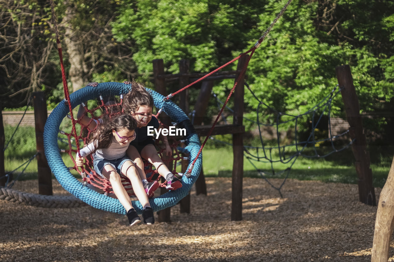 Two caucasian girls flying at speed with hair fluttering in the wind sitting on a round rope