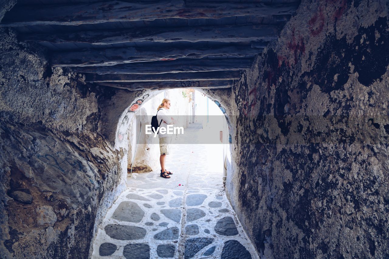 Man standing with arms crossed seen through archway in city