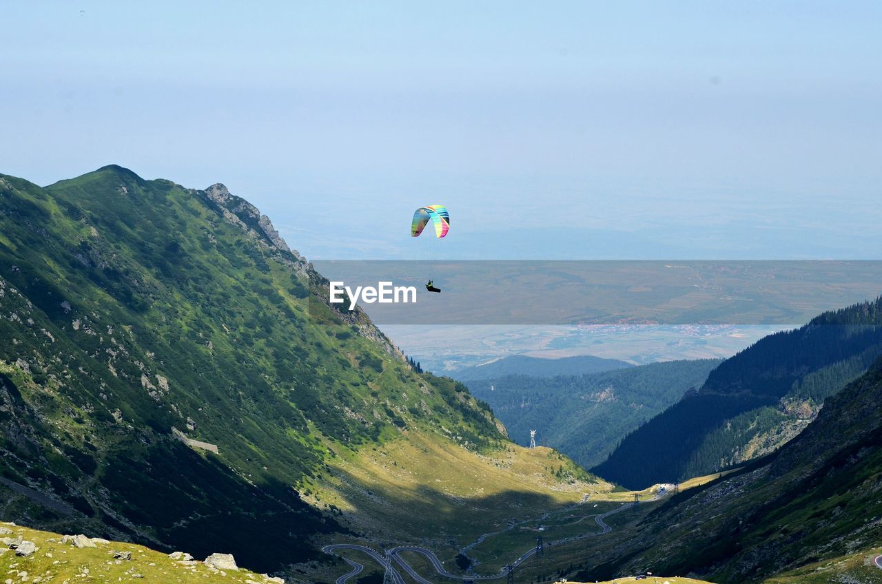 PERSON PARAGLIDING OVER MOUNTAIN AGAINST SKY