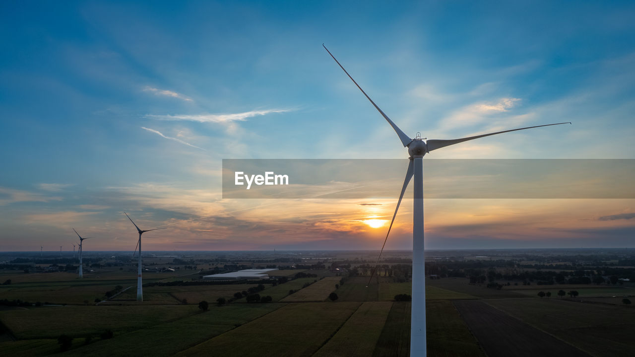 low angle view of windmills on field against sky during sunset