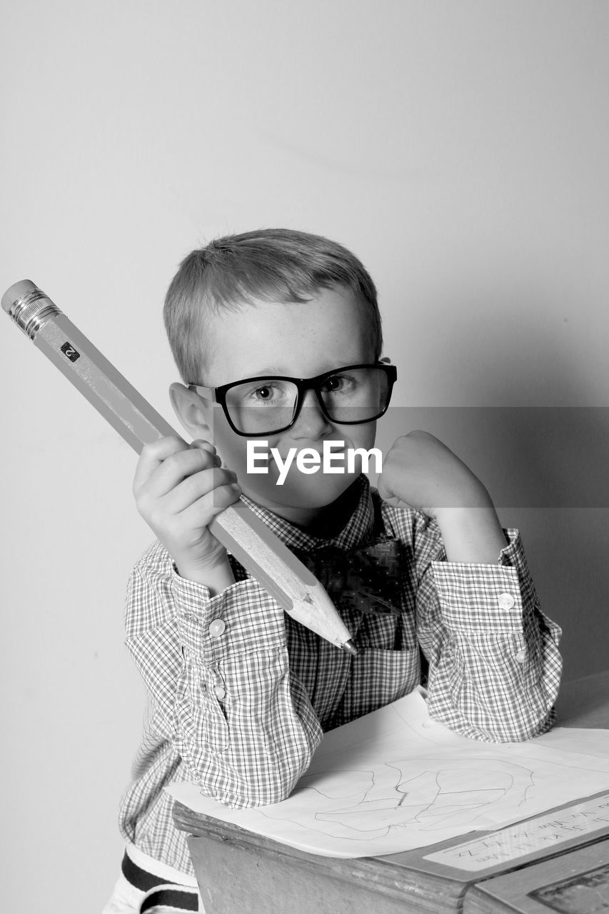 Portrait of cute boy holding pencil while sitting on desk at home