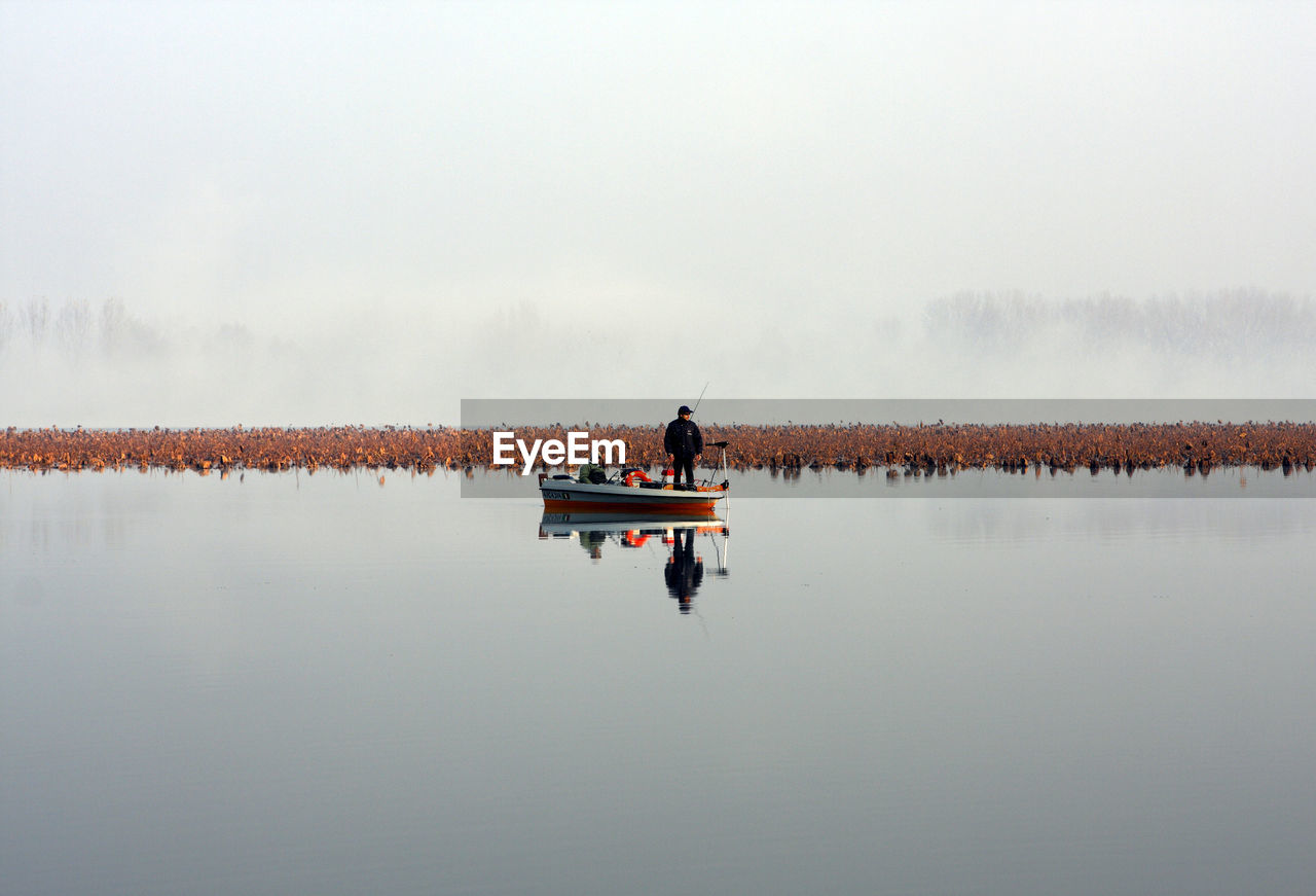 Fishermen sailing in lake against sky