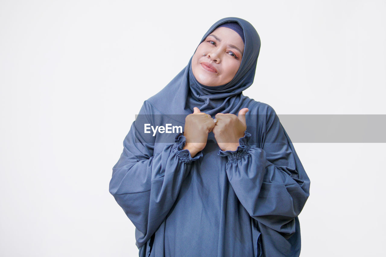 one person, studio shot, portrait, clothing, blue, adult, outerwear, indoors, hood, white background, smiling, waist up, emotion, looking at camera, hand, sleeve, happiness, women, young adult, human face, front view, hijab, scarf, cut out, headscarf