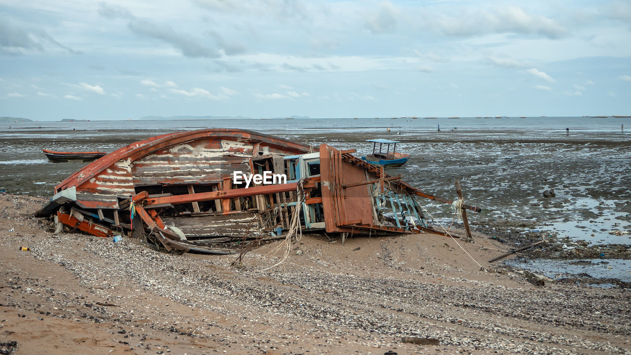 ABANDONED BOAT ON BEACH AGAINST SKY