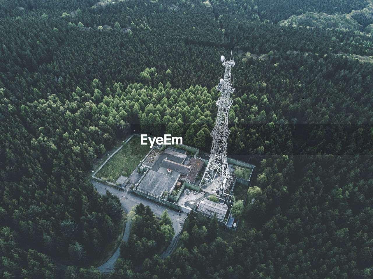 Aerial: drone shot of old abandones radio tower station in rich green forest surrounded by trees