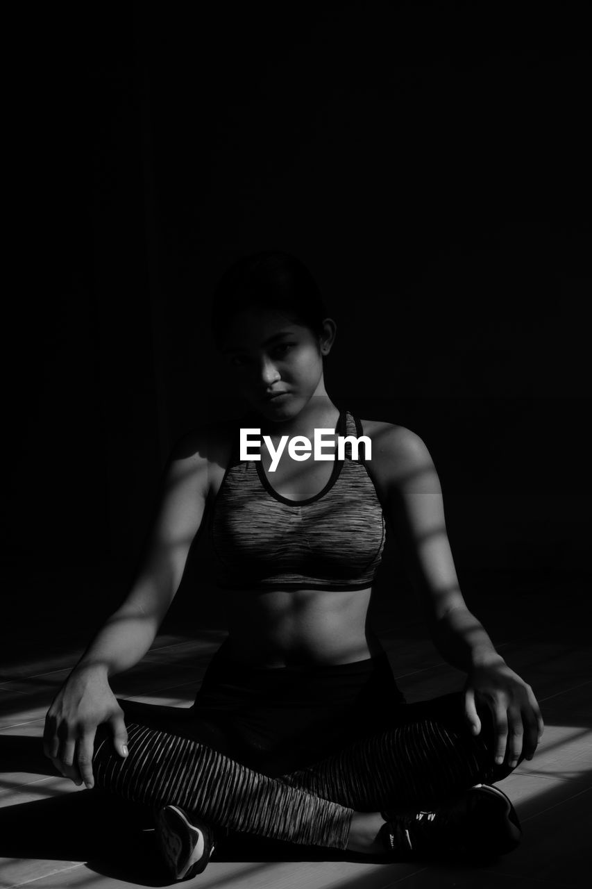 Full length of young woman relaxing while sitting on floor in darkroom at home
