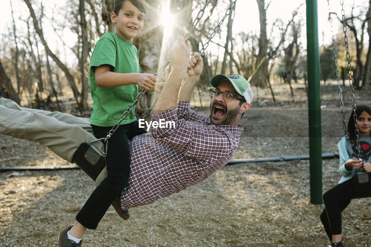 Portrait of happy family swinging against bare trees in playground