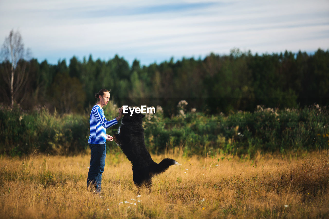 Side view of man playing with dog on grassy land