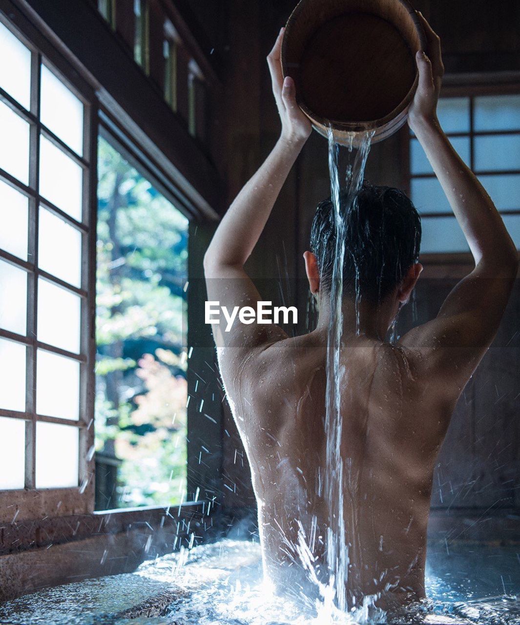 Rear view of shirtless man taking bath at home