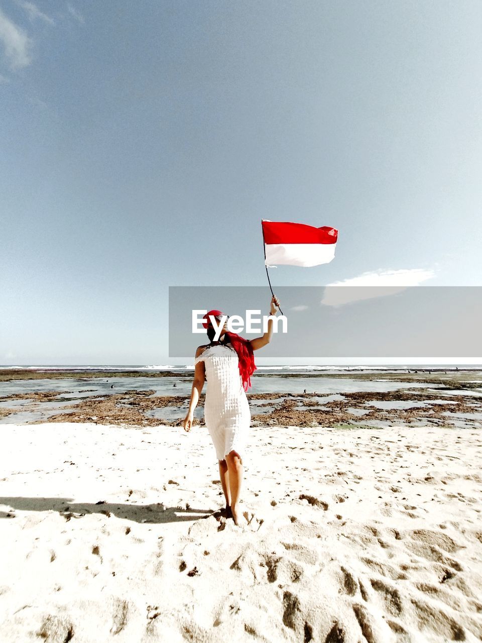 Rear view of woman walking on beach holding flag