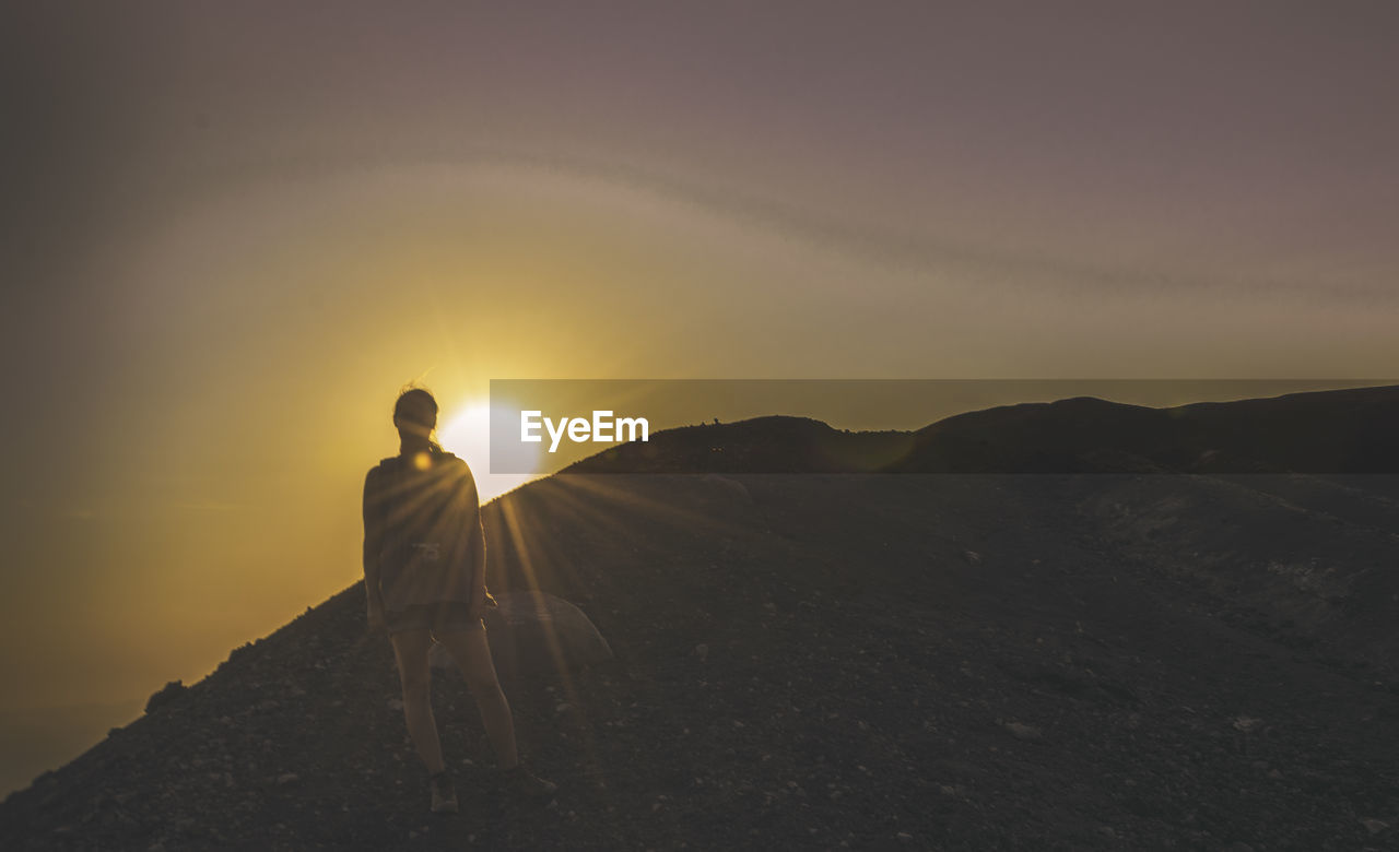 Full length of female hiker standing on mountain against sky during sunset