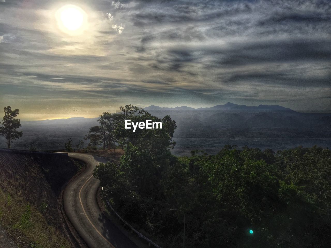 High angle view of empty road by trees on landscape against cloudy sky