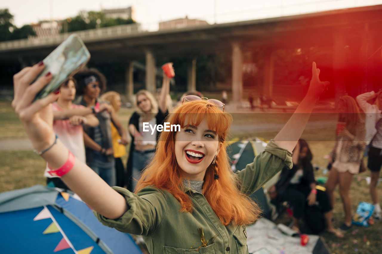 Happy young woman taking selfie with friends while camping during music festival
