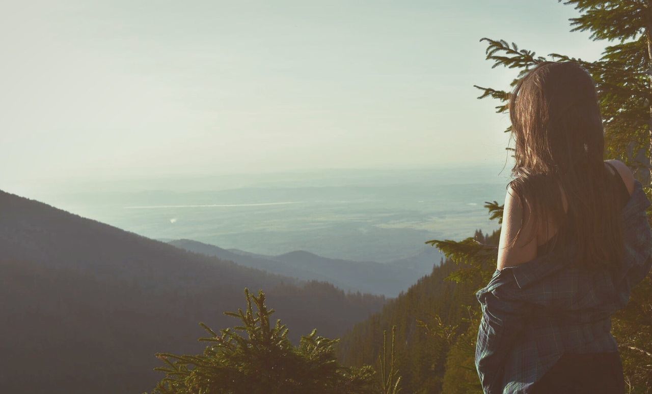 Rear view of young woman looking at view while standing on mountain against sky