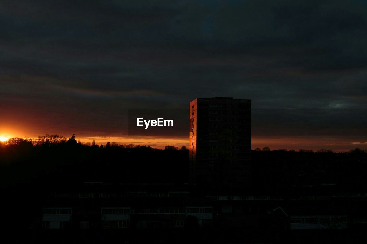 Silhouette building on field against cloudy sky