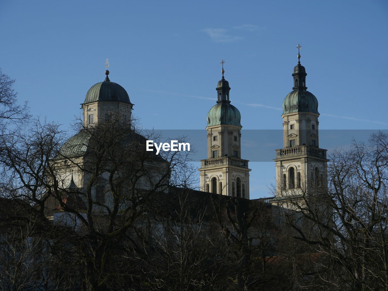 Low angle view of bare trees by st lorenz basilica against blue sky