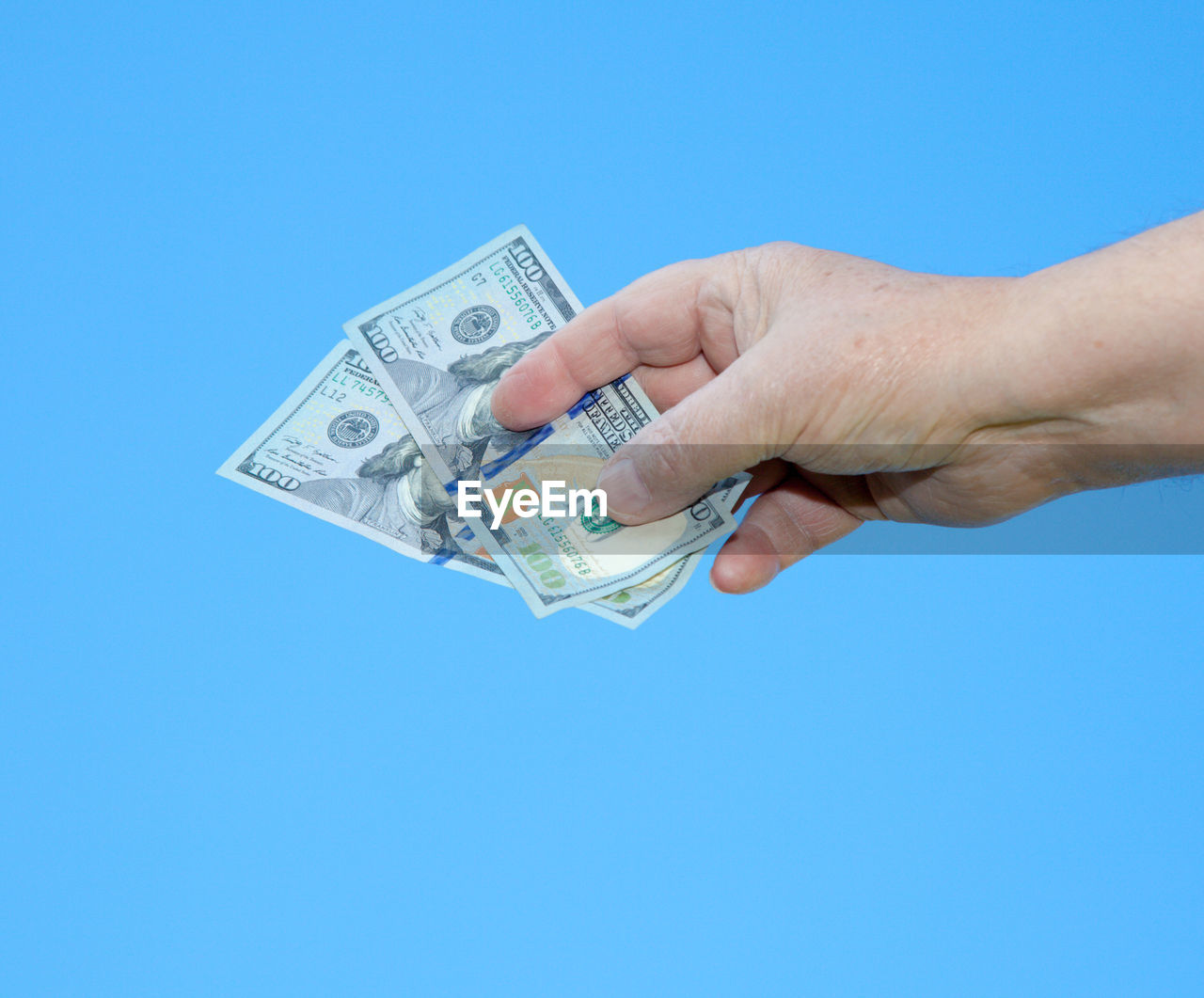Cropped hand holding us currency against blue background